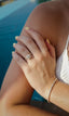 Close-up of a woman’s hand by a pool, adorned with the ‘Parasol’ diamond ring and a ‘Tennis Bracelet’, complemented by her bright yellow nail polish.