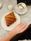 A person's hand with a diamond ring and bracelet, enjoying a croissant and hot chocolate at Angelina café.