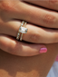 A close-up of a woman's hand featuring the 'Soleil' ring, a stunning emerald-cut diamond set between two gold bands encrusted with smaller diamonds